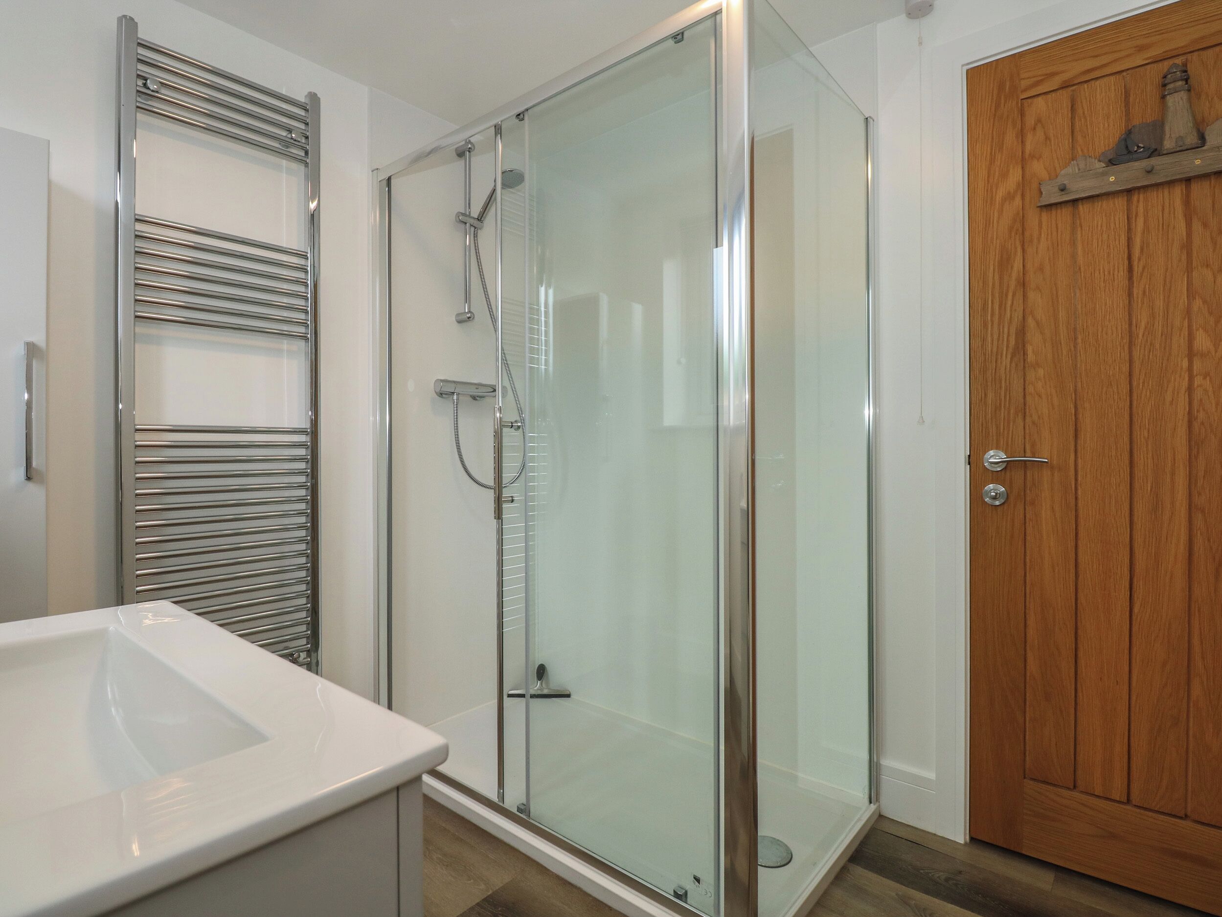 A modern bathroom with a glass shower enclosure, a white sink, and a wooden door.