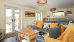 A cozy living room with a sofa, a coffee table, and a dining area. - Tawny's Roost (King's Lynn)