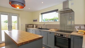 A modern kitchen with grey cabinets, a wooden countertop, a built-in oven, and a window above the sink. - Tawny's Roost (King's Lynn)