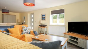 A cozy living room with a sofa, coffee table, and TV. There's a window with a view of greenery outside. - Tawny's Roost (King's Lynn)