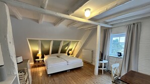 Ein Schlafzimmer mit schrägem Dach, einem Bett, einem Schreibtisch und einem Stuhl.
