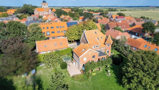 Eine Vogelperspektive auf ein Dorf mit traditionellen Häusern, einer markanten Kirche mit Turm und umliegenden grünen Feldern.