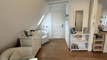 A narrow attic room with a sloped ceiling, a white door, a small white desk, a chair, and a bookshelf.