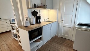 Eine kleine Küche mit weißen Schränken, einer Mikrowelle, einer Kaffeemaschine und einem Spülbecken.