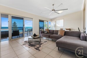 Relax in this spacious living room with a sofa, coffee table, and side table, offering a view of the ocean and a tree from the balcony.