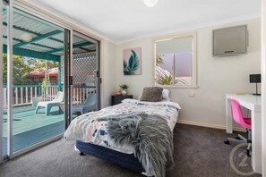 Une chambre à coucher comprenant un lit, un bureau, une chaise, un téléviseur et une porte-fenêtre coulissante donnant sur un espace extérieur.