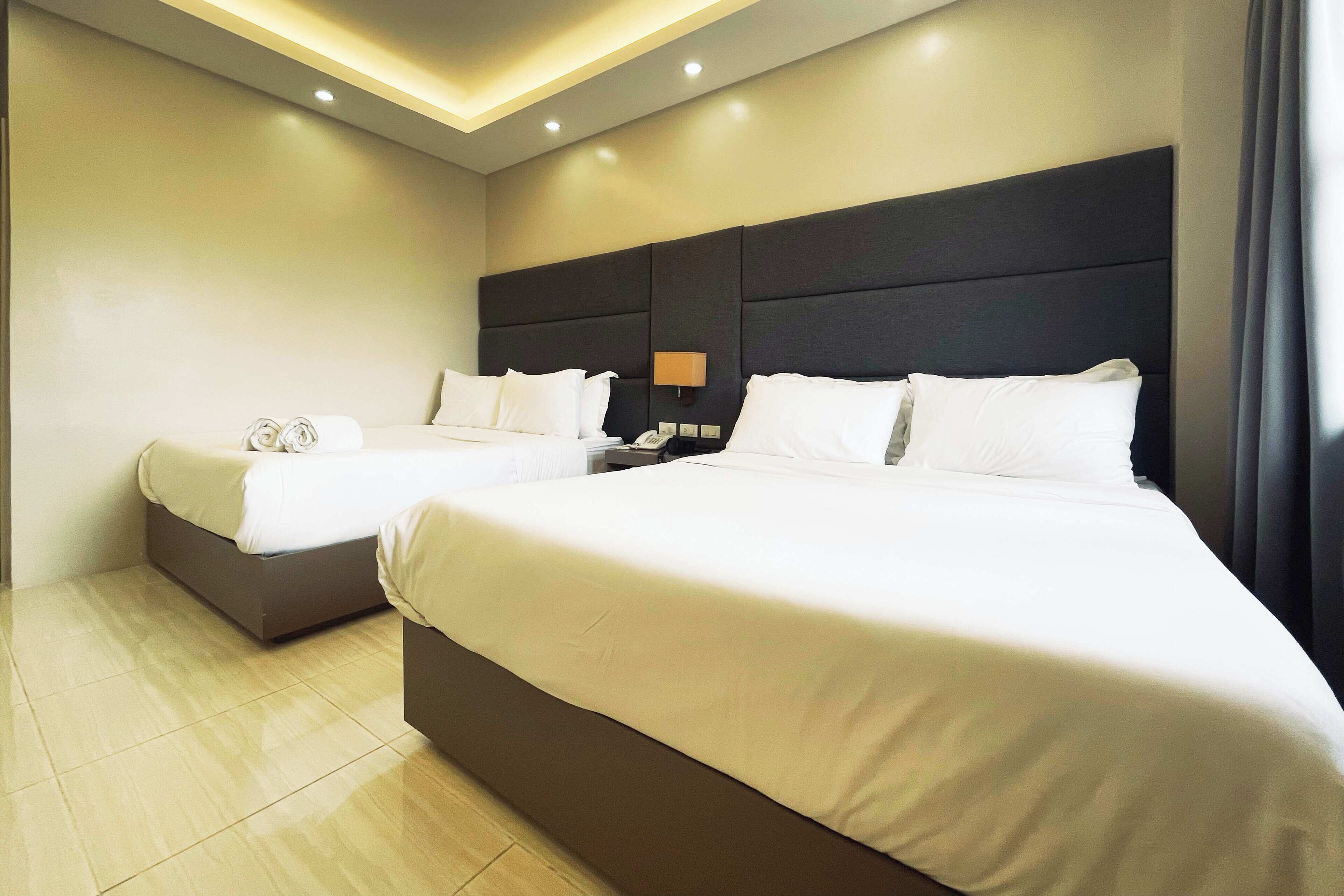 A hotel room with two beds, a nightstand with a lamp, and a modern ceiling design.