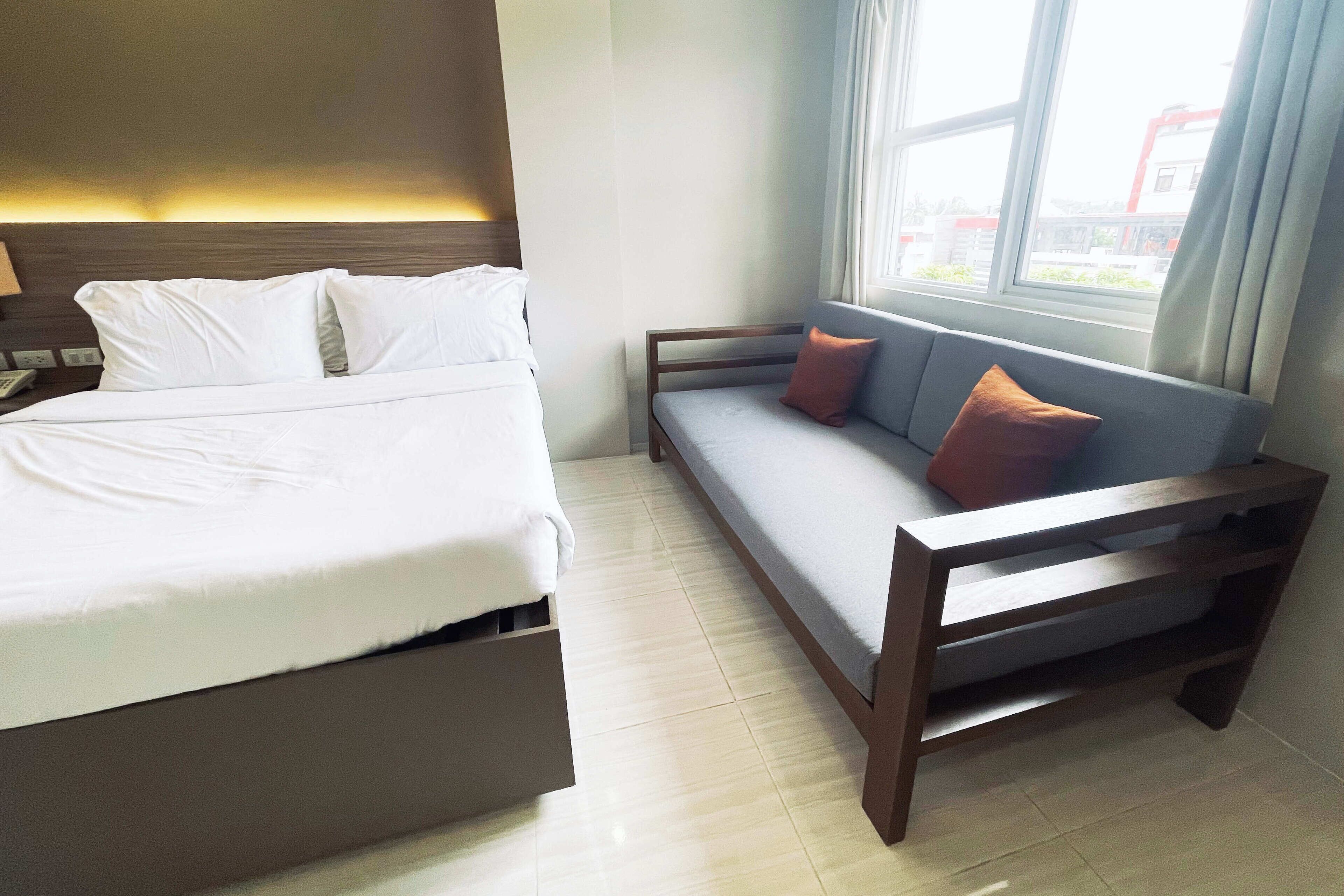 Een hotelkamer met een bed, een bank, een raam en een lamp.