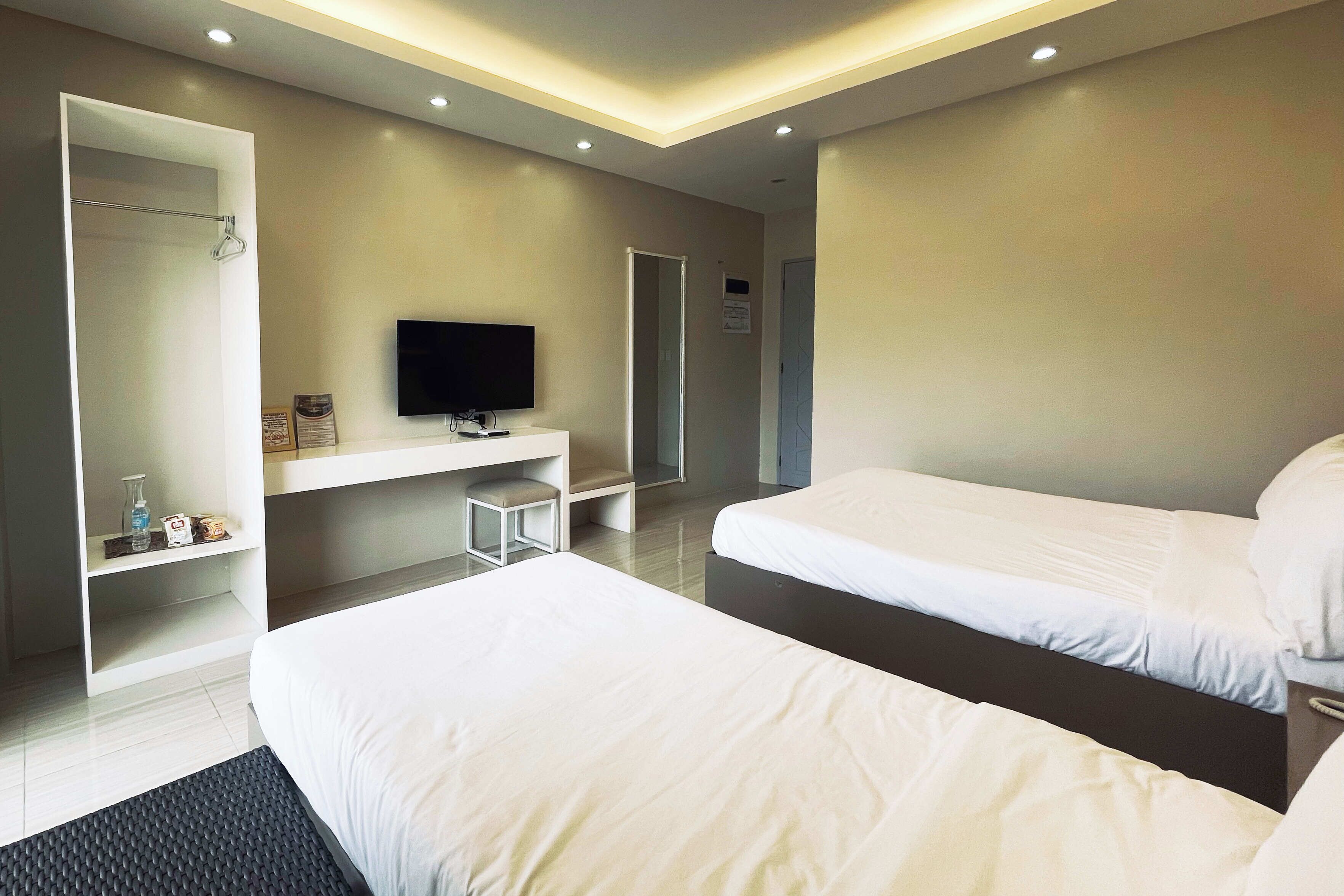 A modern hotel room with two beds, a flat-screen TV, a small seating area, and a walk-in closet.