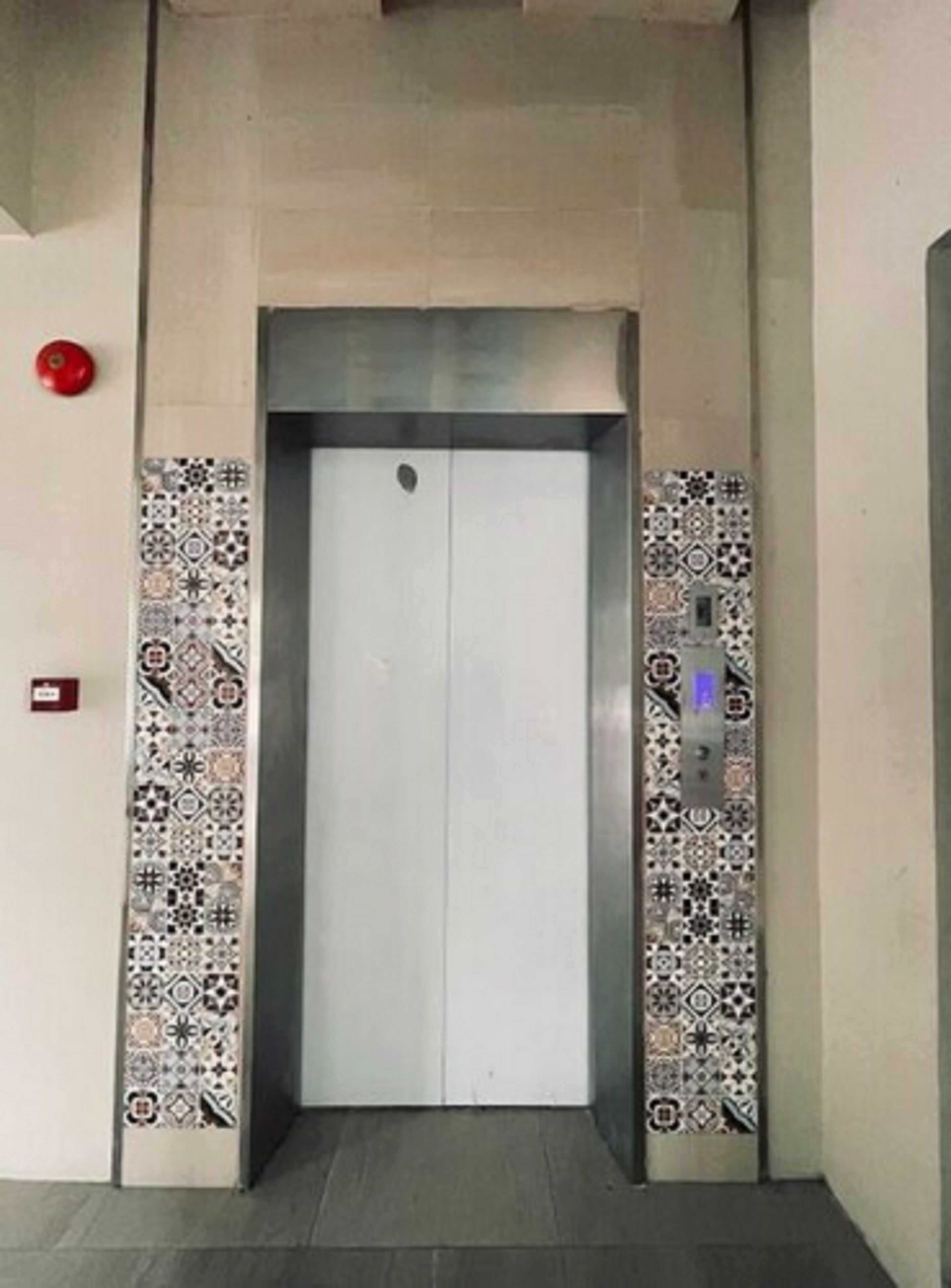 An elevator with patterned tiles on the walls and a red emergency button above it.