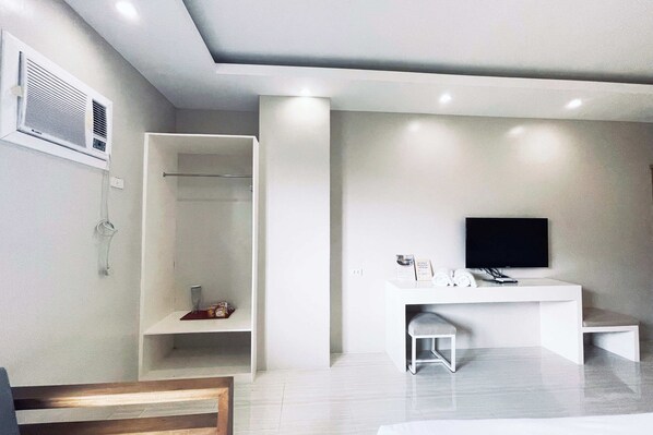 Una habitación moderna y minimalista con armario empotrado, televisor de pantalla plana y un pequeño rincón de descanso.