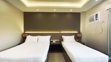 A hotel room with two single beds, a small bedside table with a phone, and a wall-mounted air conditioning unit.