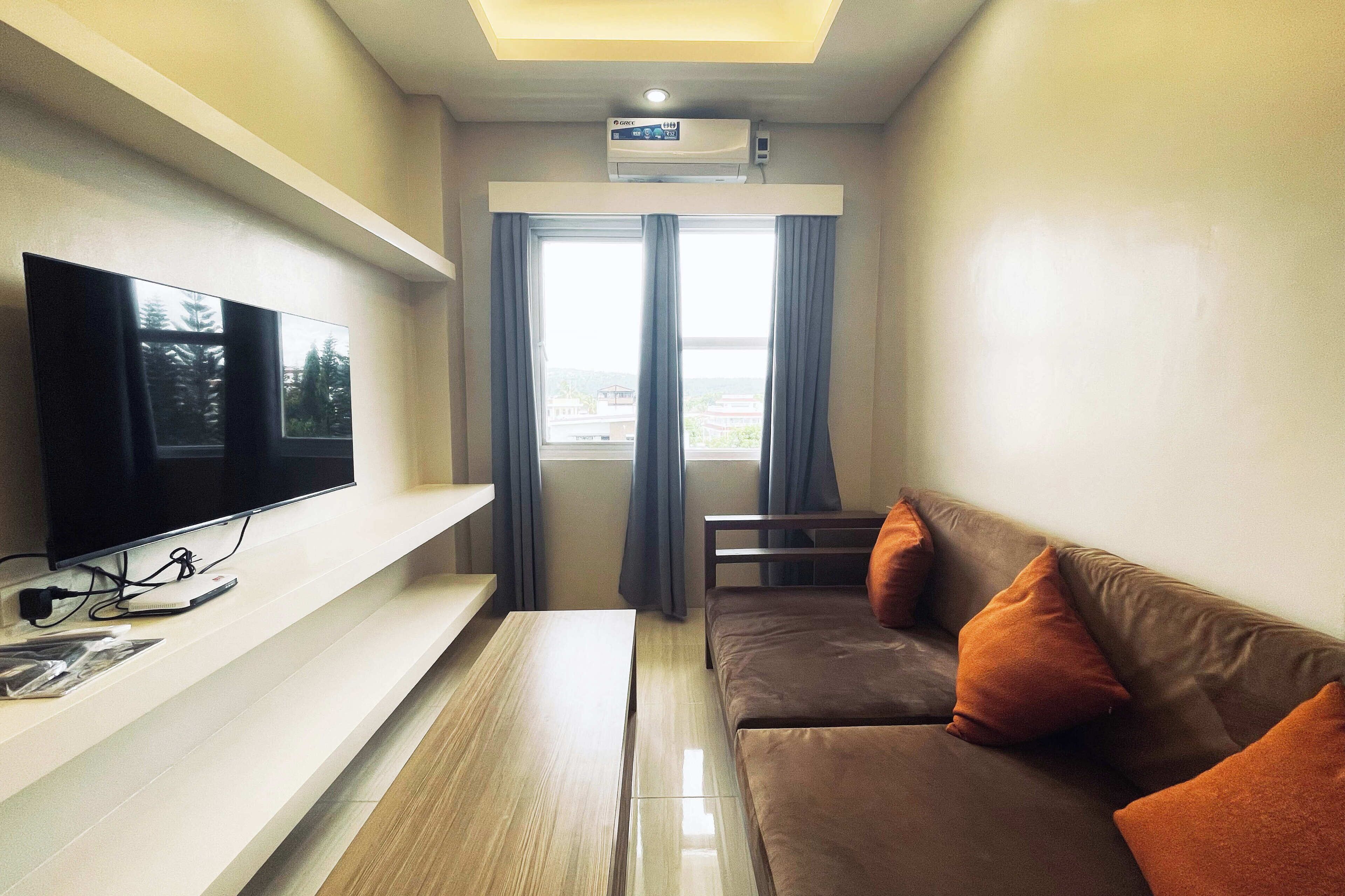Uma sala de estar moderna com uma TV de tela plana, um sofá com almofadas laranja, uma mesa de centro de madeira e uma janela grande com cortinas.