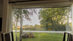 En utsikt från ett fönster med ett bord och stolar, med utsikt över en gräsyta med träd och en väg.
