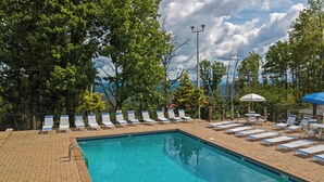 Ein Schwimmbecken mit Liegestühlen und Sonnenschirmen, umgeben von Bäumen und einem bewölkten Himmel.