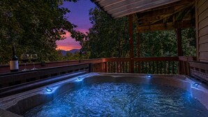 Ein Whirlpool mit Holzterrasse und Blick auf Bäume und Berge bei Sonnenuntergang.