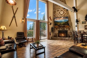 A spacious living room with a fireplace, leather furniture, and a large window offering a view of the outdoors.