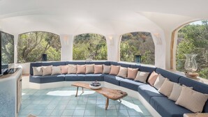 A modern living room with a curved sectional sofa, a wooden coffee table, and large arched windows offering a view of the outdoors.