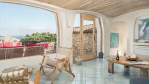A spacious balcony with wicker furniture, a stone wall, and a view of the sea.