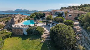 A villa with a swimming pool, stone architecture, and a view of the sea.
