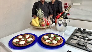 A kitchen with two pizzas on blue plates, a fruit bowl with bananas and pineapple, a champagne bottle, and a fish decoration on the wall. - Villa in Porto Rotondo with 7 bedrooms sleeps 14 (Porto Rotondo)