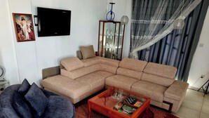 A living room with a sectional sofa, a round coffee table, and a blue armchair. - Impeccable 3-bed Villa in Nicosia (Agia Varvara)