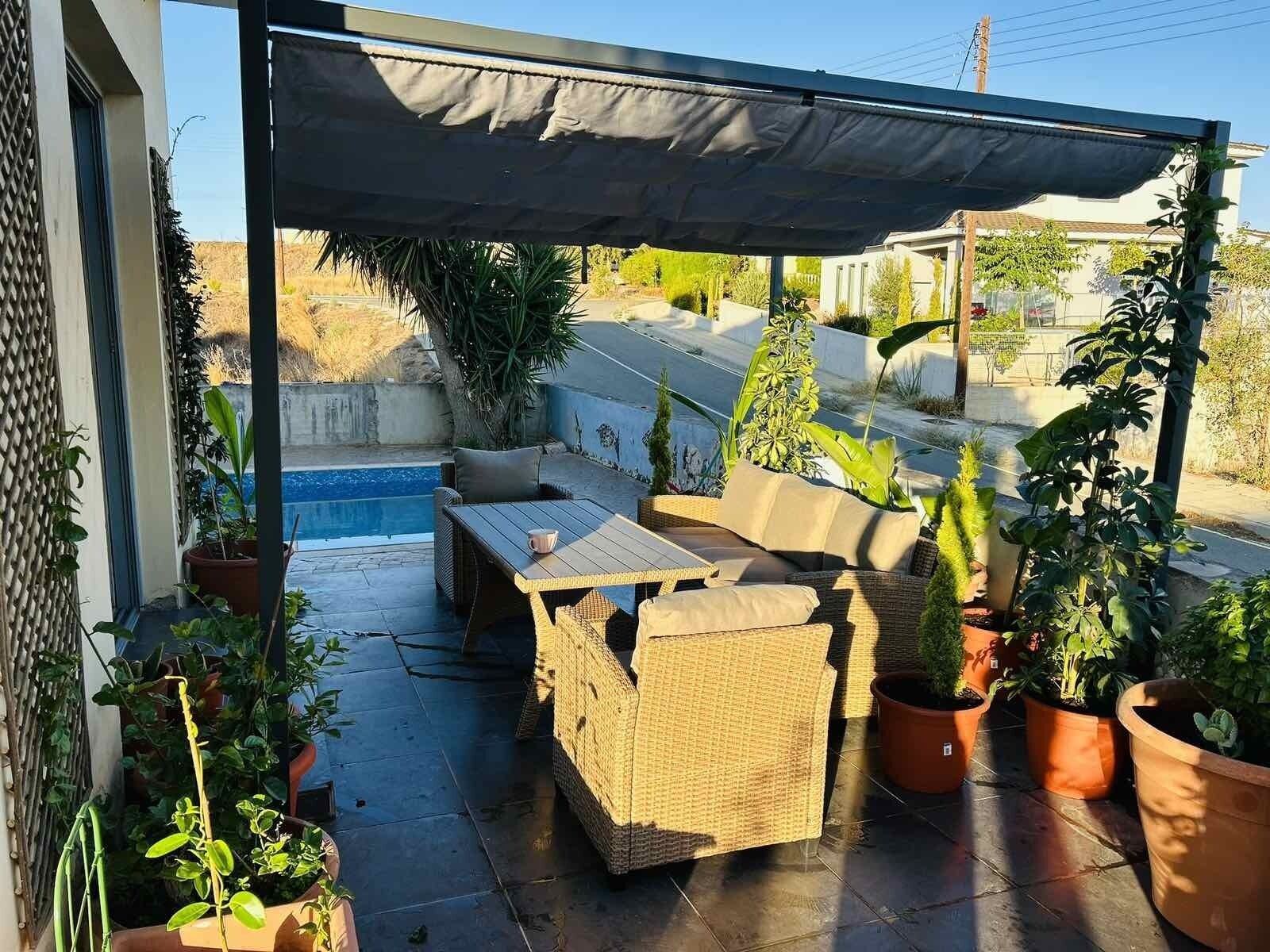 A covered patio area with outdoor furniture, a pool, and potted plants.