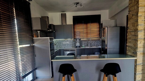 A modern kitchen with a central island, two bar stools, and a stone accent wall. - Impeccable 3-bed Villa in Nicosia (Agia Varvara)