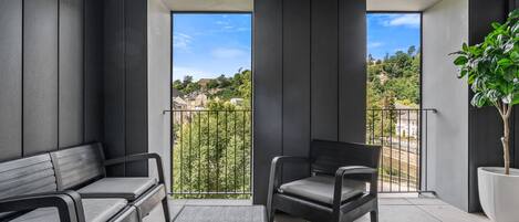 A modern balcony with a sofa, armchair, and potted plant, offering a view of a residential area.