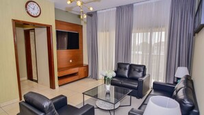 A modern living room with a sofa set, a coffee table, a TV mounted on the wall, and a large window with curtains. - Robyson Residency Kinshasa (Kinshasa)