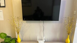 Moderni olohuone, jossa seinälle on asennettu taulutelevisio, huoneessa on puinen työpöytä, jossa on valkoinen laatikko, sekä kaksi keltaista maljakkoa, joissa on koristeellisia oksia.