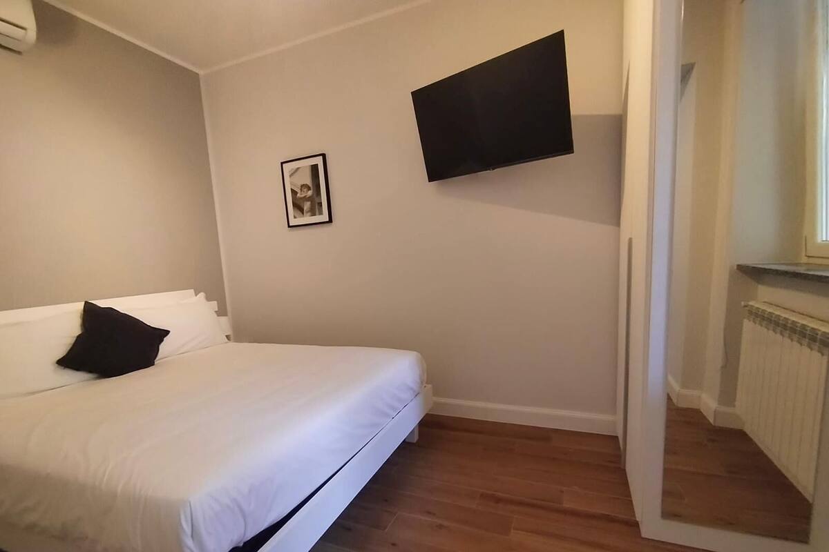 A bedroom with a bed, a flat-screen TV mounted on the wall, a framed picture, and a radiator.