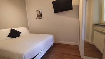Un dormitorio con una cama, un televisor de pantalla plana montado en la pared, un cuadro enmarcado y un radiador.