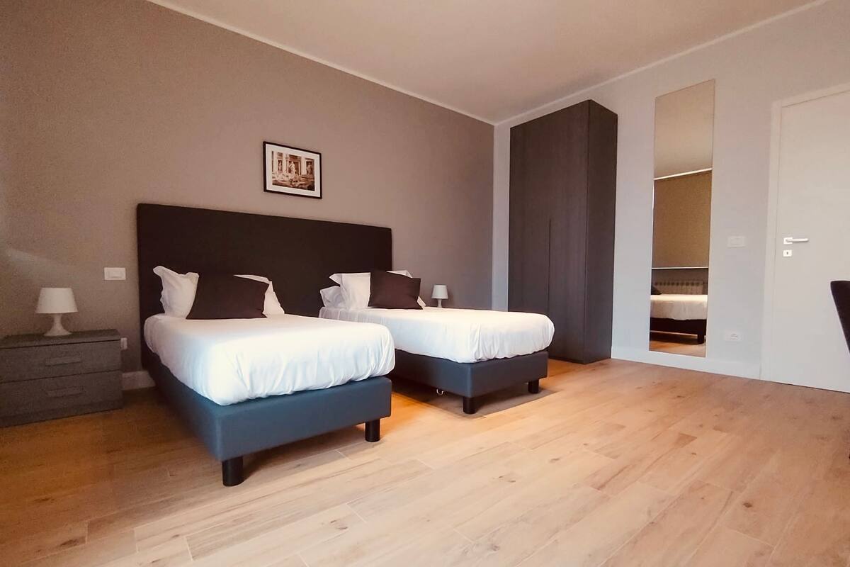 A modern bedroom with two beds, a dark headboard, and a wooden floor.