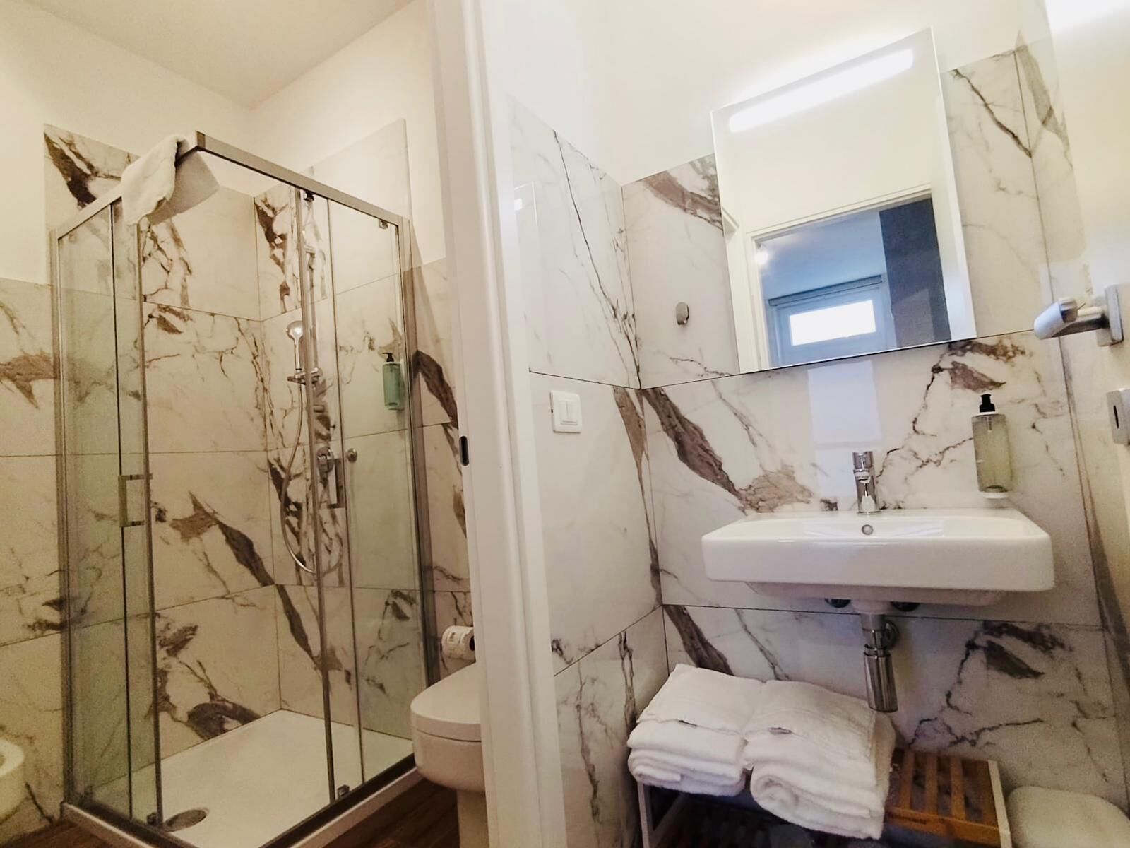 Ein Badezimmer mit einer gläsernen Duschkabine, einem weißen Waschbecken und einer Wand mit Marmorfliesen.