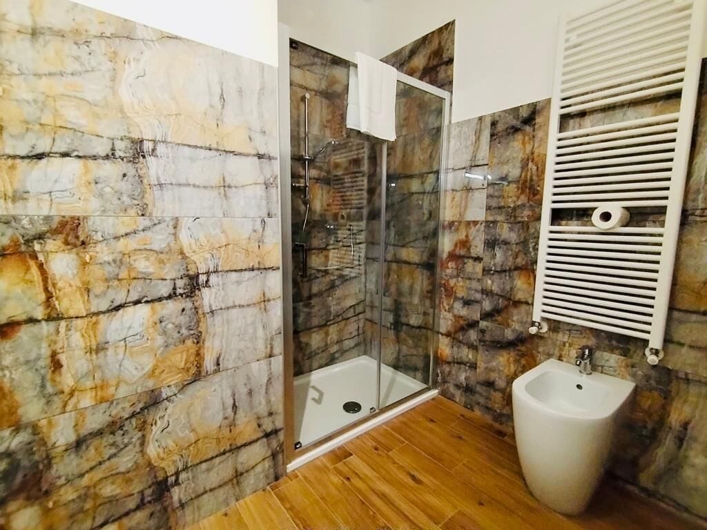 A bathroom with a glass-enclosed shower, a bidet, and marble walls.