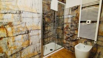 A bathroom with a glass-enclosed shower, a bidet, and marble walls.
