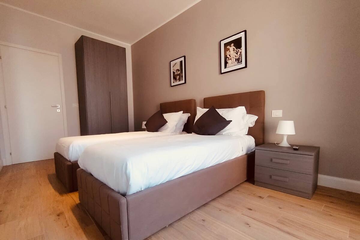 A bedroom with a large bed, a nightstand, a wardrobe, and two framed pictures on the wall.