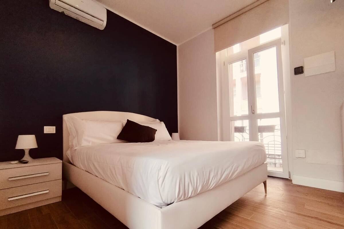 A bedroom with a bed, a nightstand, a lamp, and a window with a view.