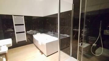 A modern bathroom with a glass-enclosed shower, a white bathtub, and a wooden floor.