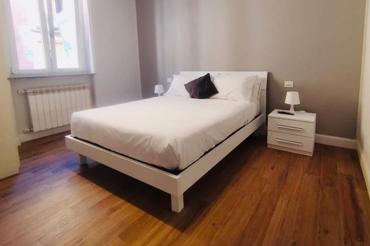 Une chambre à coucher avec un lit, une table de chevet, une lampe et une fenêtre.