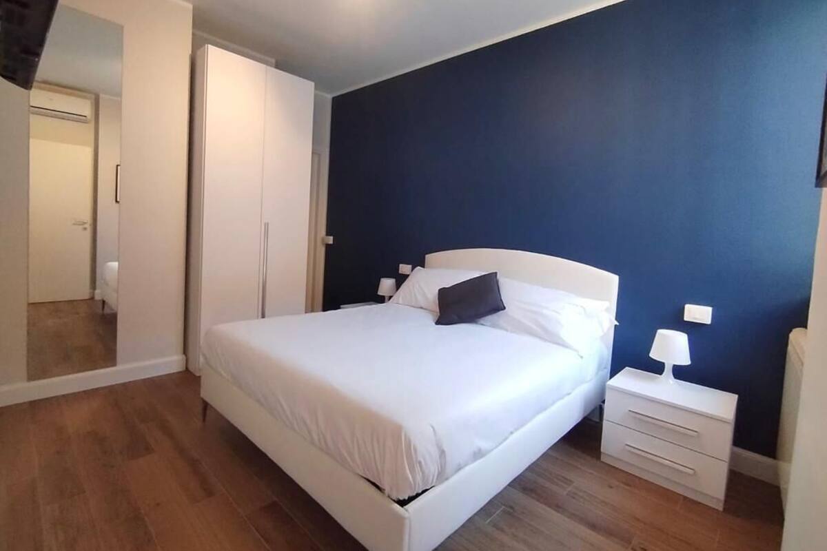 Une chambre avec un lit blanc, une table de chevet et un mur bleu.