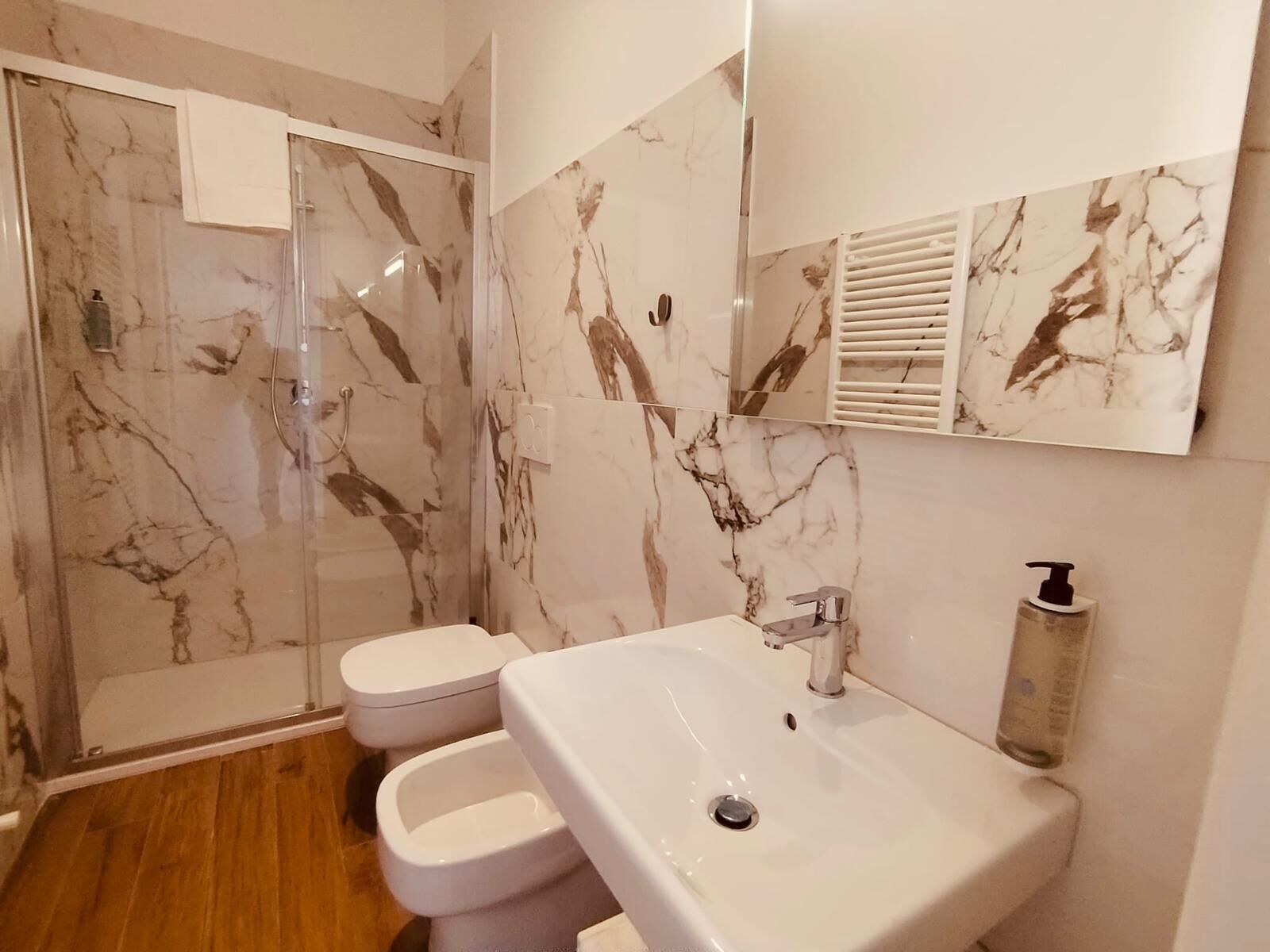 A bathroom with a glass-enclosed shower, a white sink with a soap dispenser, and marble-patterned walls.