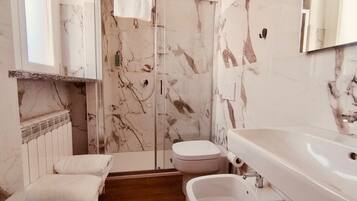 Un bagno con doccia in marmo, un water, un bidet e un lavandino.