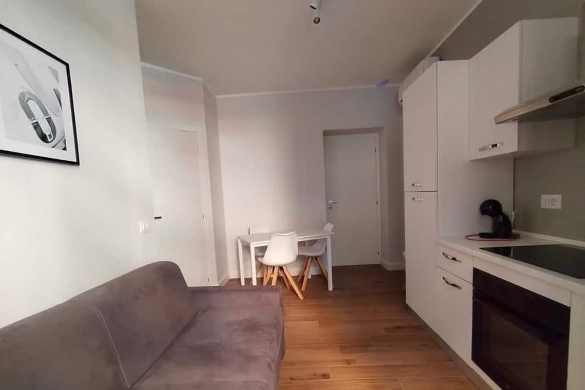 Un espace de vie compact comprenant un canapé, un coin repas avec une table et des chaises, et une kitchenette équipée de placards et d’un four.