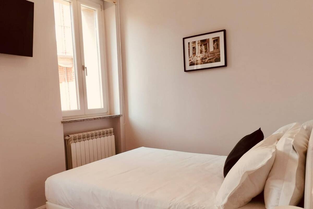 A bedroom with a bed, a radiator, a window, and a framed picture on the wall.