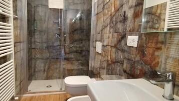 Ein modernes Badezimmer mit einer begehbaren Glasdusche, zwei Toiletten und einem großen Waschbecken.