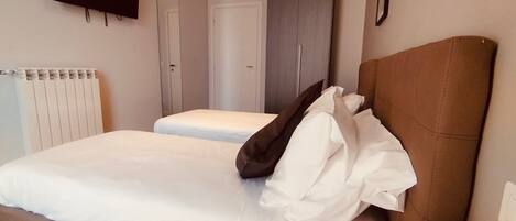 Un dormitorio con cama, televisión montada en la pared, armario y radiador.