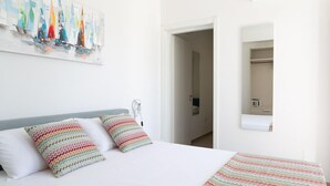 Habitación de hotel con cama, almohadas coloridas, un cuadro de veleros y vista a un armario y baño.
