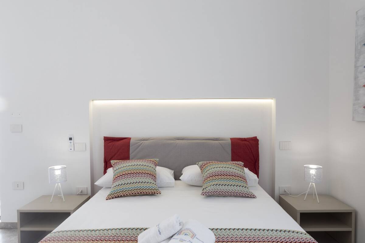 A modern hotel room with a large bed, two bedside tables, and a headboard with integrated lighting.